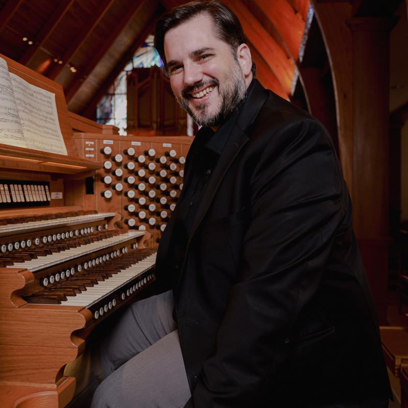 Bradley, seated at a large organ, smiling at the camera